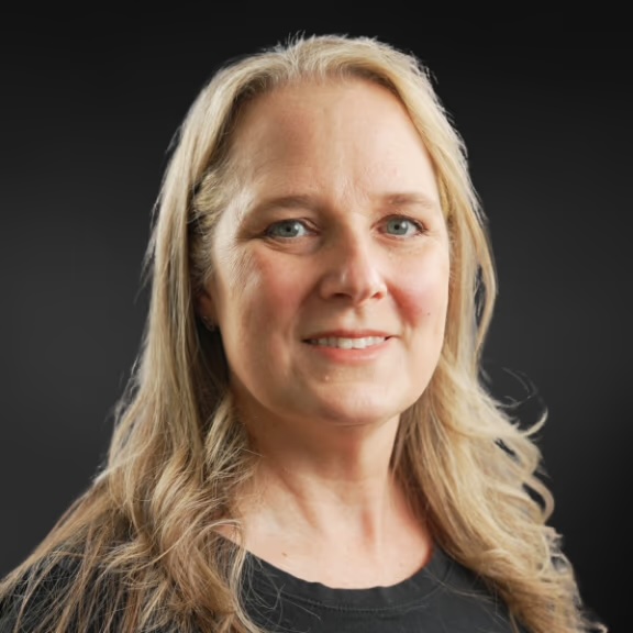 The image features a woman with medium-length hair, wearing a black top, posing against a dark background.