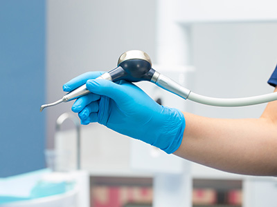A medical professional wearing blue gloves holds a device with a long tube over an object on a table.