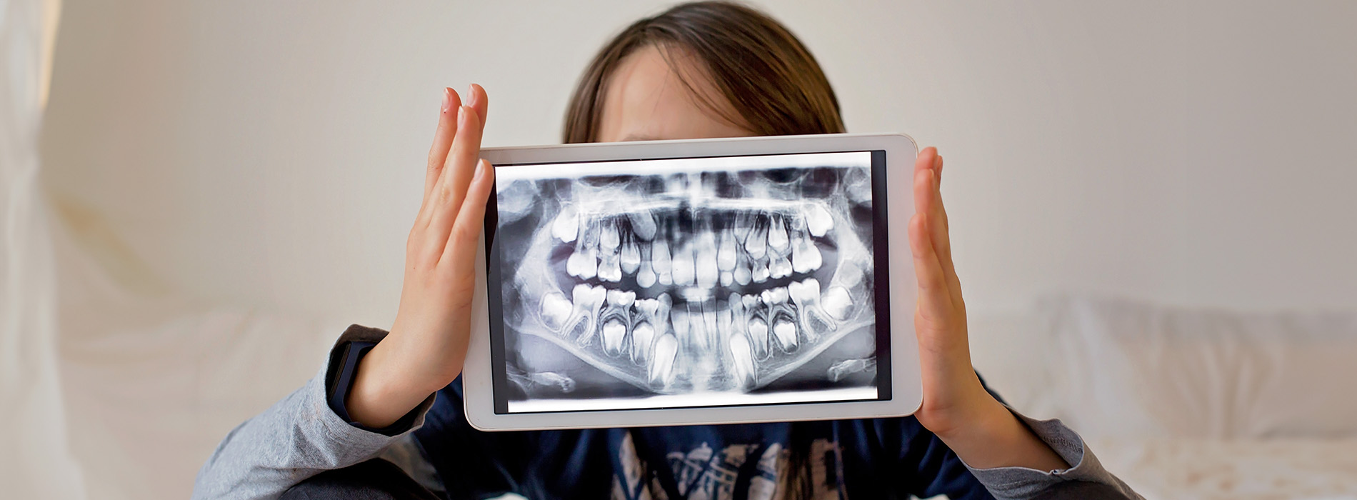 A child holding up three tablets showing images of teeth, with their reflection visible on the devices screens.