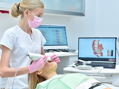 A dental hygienist using an ultrasonic scaler on a patient s teeth while another person operates a computer screen.