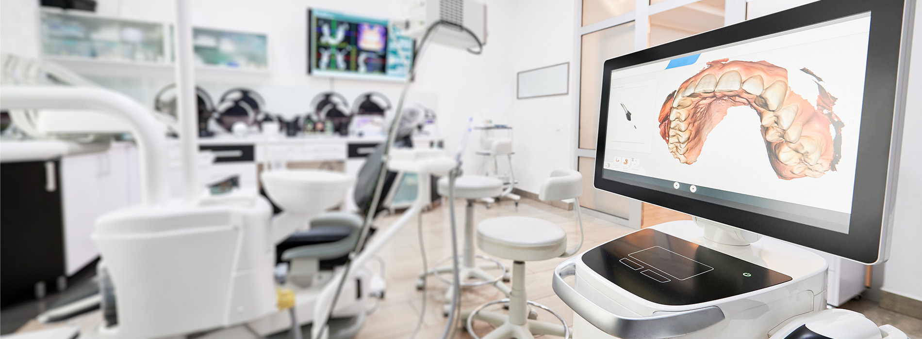 The image depicts a modern dental office with various pieces of equipment and a large screen displaying an image of a mouth.