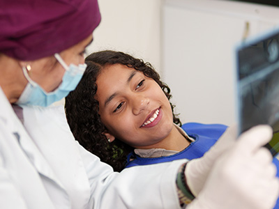 The image shows two individuals wearing white lab coats, with one person smiling at the camera while looking at a microscope slide, and another person standing behind them, observing the first s work.
