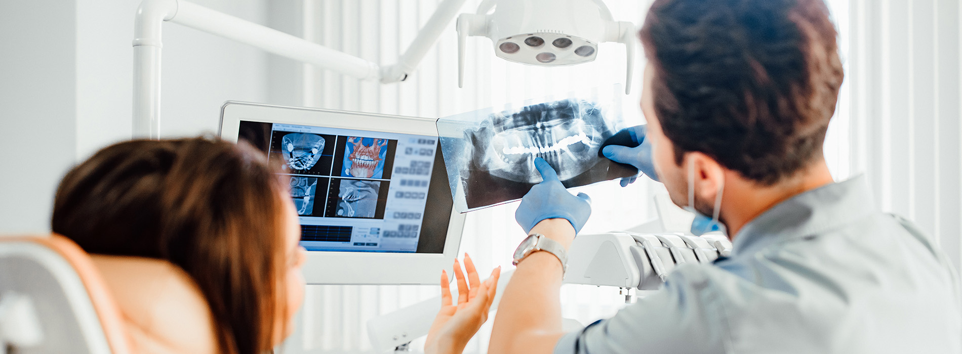 An image shows two people in a medical setting, with one person sitting at a desk looking at a laptop screen displaying medical images, while another stands behind them, observing the same screen.