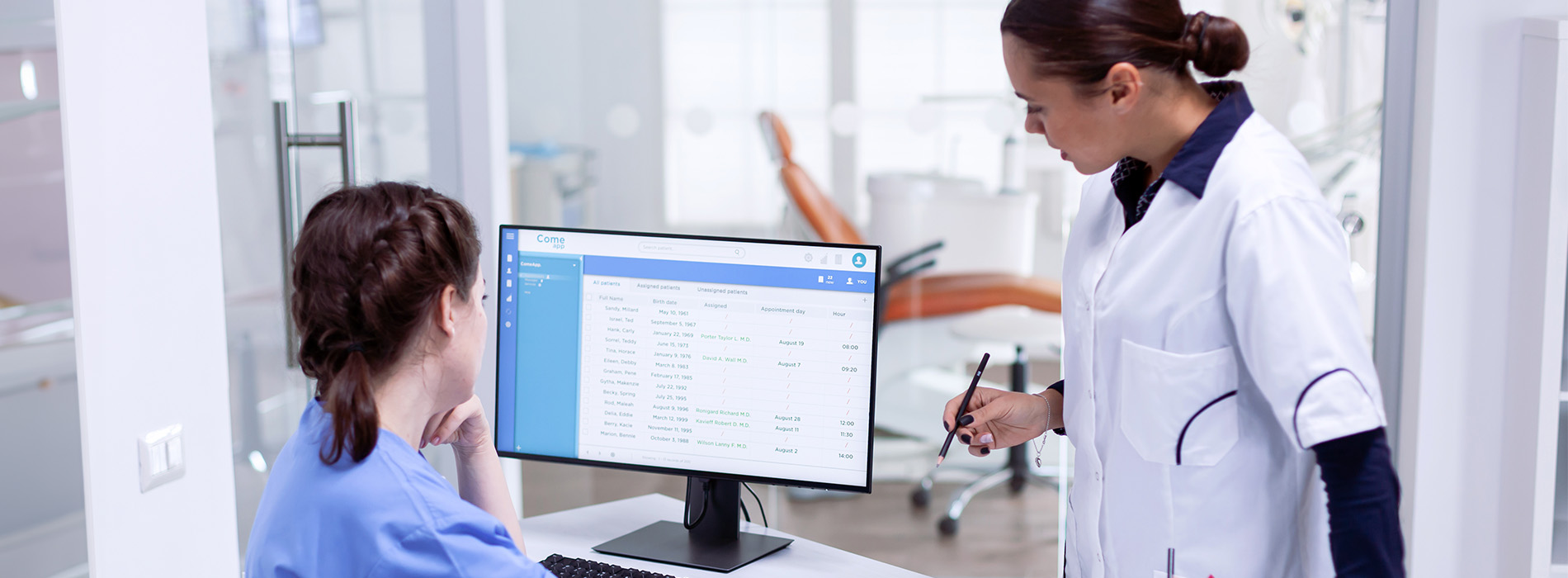 An image depicts two individuals in a medical setting, with one person standing at a desk and another seated, both engaged in an activity on a computer screen.