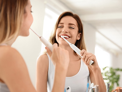 The image shows a woman brushing her teeth while another woman looks on with a smile.