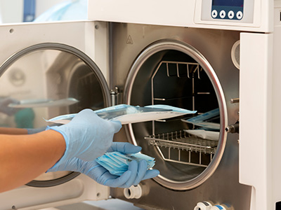 A person wearing gloves is loading laundry into an industrial washing machine.