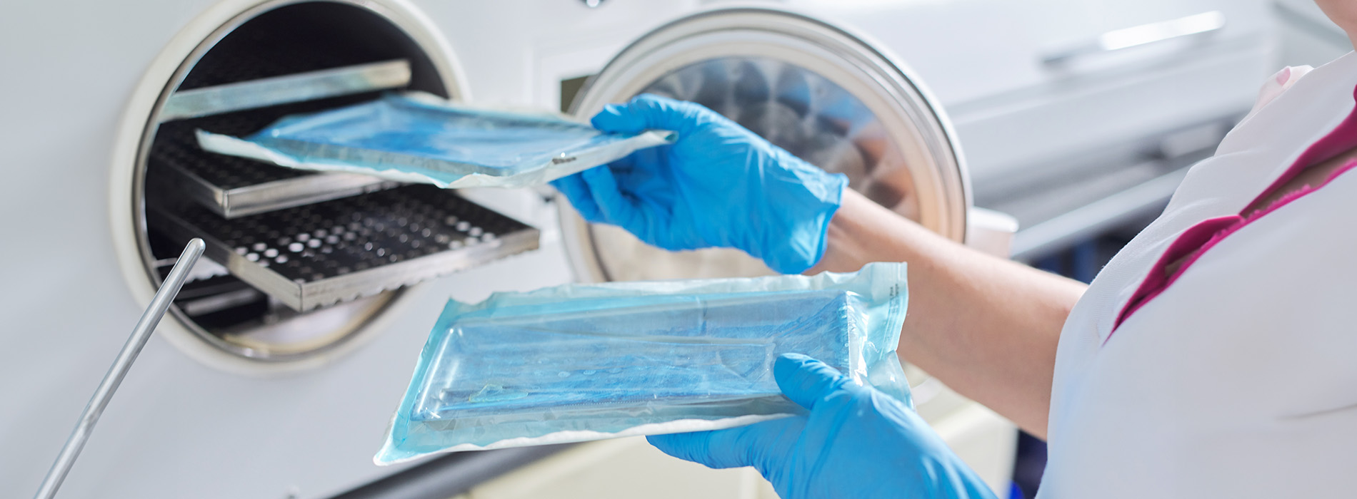 A person wearing blue gloves and a white coat is handling a large plastic bag containing a clear substance, possibly in a laboratory setting.