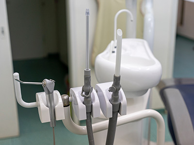 An image shows a dental chair with various medical equipment attached to it, including a handheld suction device and a dental tool holder.