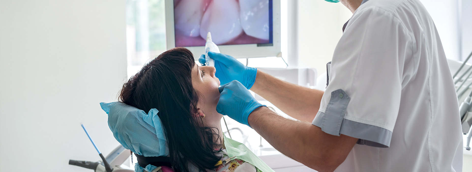 The image shows a dental professional attending to a patient in a dental chair, with the professional adjusting the patient s mouth using a tool.