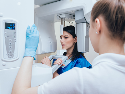 A woman in blue standing next to a large white scanner with a digital display, and another woman in a white shirt looking at her through the scanner s viewer.