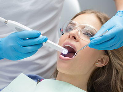 A woman receiving dental care with a dentist using a device to scan her teeth.