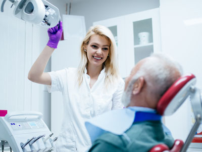 Woman standing next to man sitting in dental chair, both in medical setting.